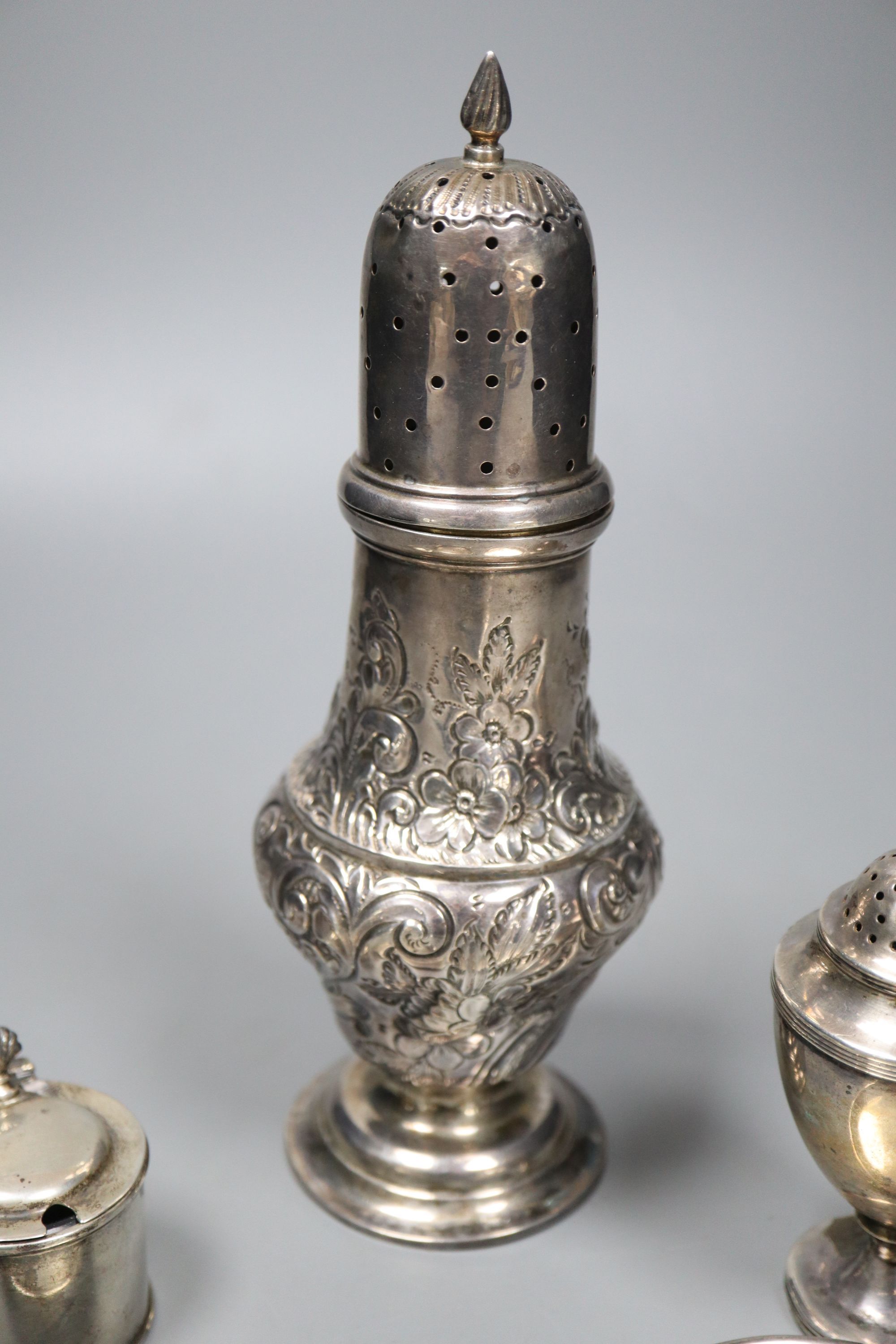 An Edwardian embossed silver sugar caster, 21.2cm, a small Georgian caster, a silver mustard and two circular pin dishes,
